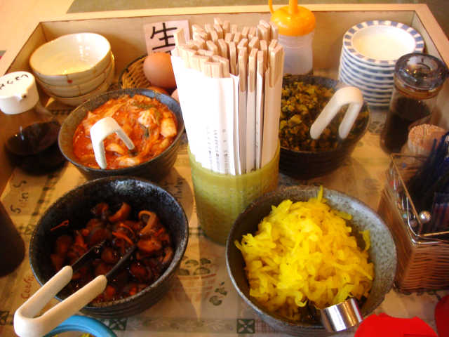 テーブルの真ん中には、生卵、味付海苔、キムチ、高菜などが置かれている。